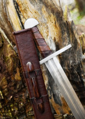 Épée normande à pommeau en demi-lune – SK-C, acier gris et cuir brun, vue au fourreau sur tronc, reconstitution GN et LARP