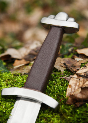 Détail poignée cuir brun et garde droite de l’épée viking Wheeler VI SK-C, posée sur mousse en sous-bois, pour GN et scène