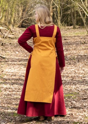 Vue de dos du tablier viking Tinna jaune, porté sur une robe rouge avec coupe ouverte et dos droit