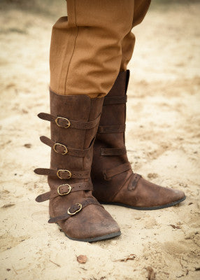 Bottes médiévales marron en cuir suédé portées de face, cinq boucles en laiton, silhouette marquée adaptée à une tenue historique