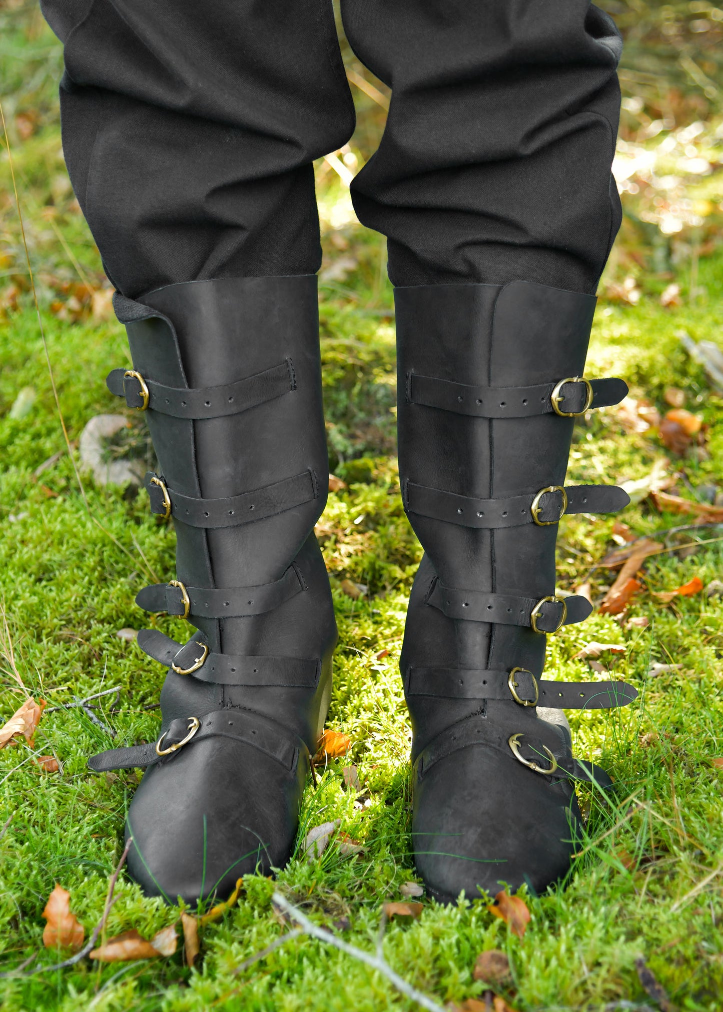 Bottes médiévales noires portées en situation complète, cinq boucles en laiton, adaptées à costume de garde ou voyageur