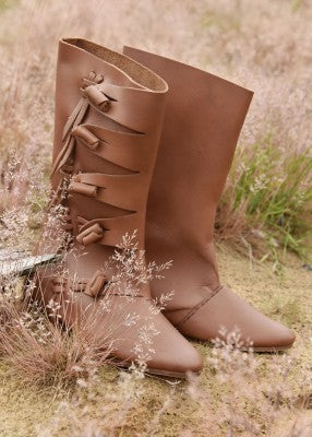 Paire de bottes vikings marron posée dans l’herbe, avec tiges hautes et fermeture latérale en cuir