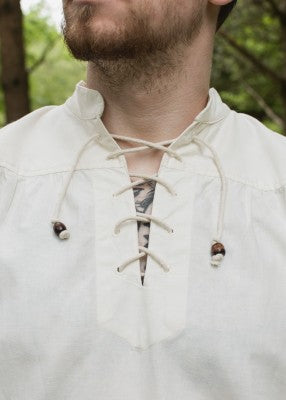 Détail de l’encolure lacée de la chemise Ludwig naturelle, avec cordons clairs et perles en bois
