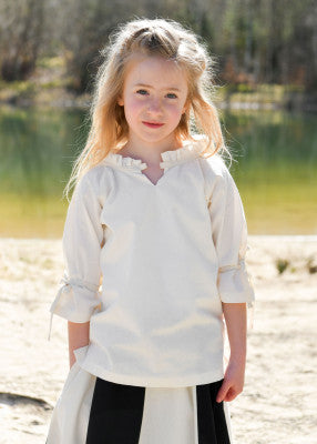 Chemisier Birga pour enfant en coton blanc, porté de face au bord de l’eau avec encolure froncée pour reconstitution, GN ou LARP enfant