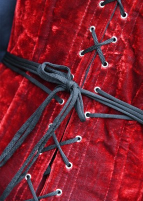 Détail du laçage du corsage pleine poitrine en velours rouge, avec œillets métalliques noirs