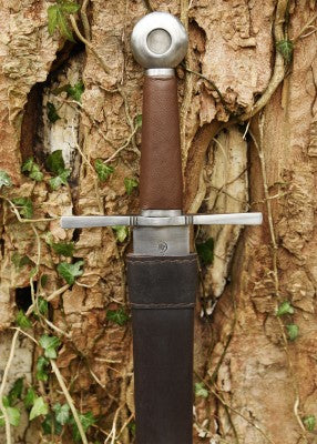 Épée d’armes à pommeau en roue – poignée brune et garde droite – épée au fourreau cuir noir, gros plan contre écorce brute