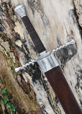 Épée bâtarde à pommeau en coquille cannelée – garde torsadée poignée brune, fourreau cuir – vue rapprochée contre tronc clair