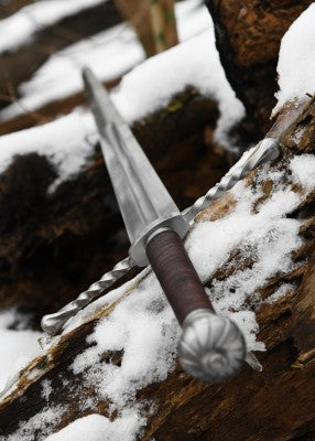 Épée bâtarde à pommeau en coquille cannelée – lame en perspective sur bûche – garde torsadée, neige en forêt, scène médiévale