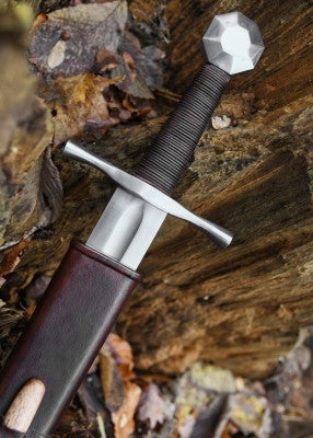 Épée de croisé à pommeau octogonal – poignée brune enroulée et pommeau acier – gros plan à l’entrée du fourreau, sur bois