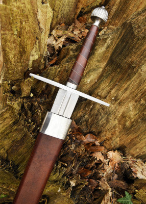 Épée longue à pommeau en poire cannelée – poignée brune et garde droite – gros plan à l’entrée du fourreau, sur bois humide