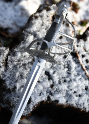 Épée en osier Mortuary – SK-B, métal gris et cuir noir, vue plongeante lame et garde panier sur rocher enneigé, GN et LARP