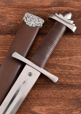 Détail épée viking Petersen S SK-B avec fourreau cuir brun, poignée gainée, garde droite et pommeau typé, photo sur bois