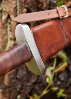 Épée viking à pommeau en disque étagé, métal gris et cuir brun, détail garde et poignée, fourreau visible, combat scénique