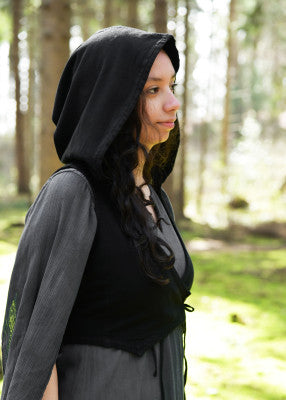 Gilet à capuche Nalen noir porté de profil, avec capuche relevée et coupe croisée sur robe grise