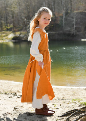 Robe Lilou pour enfant en coton orange, portée de profil en extérieur avec fente latérale pour reconstitution, GN ou LARP enfant