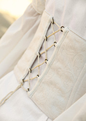 Gros plan sur le corsage blanc damassé de la robe Fine, avec œillets métalliques et laçage latéral réglable