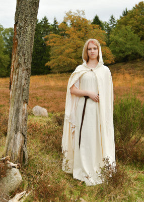 Robe médiévale Ingrid écru portée avec cape, coton léger, silhouette féminine longue, manches trompettes fendues visibles