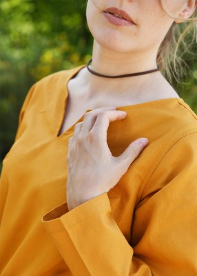 Robe médiévale Milla orange – gros plan encolure fendue, main sur le col, tissu sergé coton léger, détail couture et manches