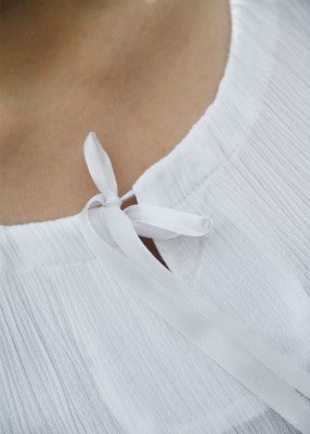 Détail de l’encolure de la sous-robe légère blanche, avec ouverture et ruban satiné blanc à nouer