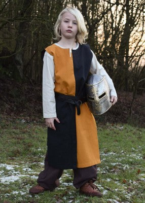 Tabard bicolore pour enfant en coton orange-noir, porté de face avec casque sous le bras pour reconstitution, GN ou LARP enfant
