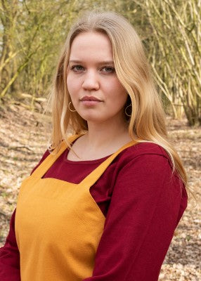 Détail du haut du tablier viking Tinna jaune, porté sur une robe rouge avec larges bretelles