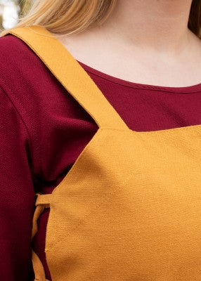 Détail du buste du tablier viking Tinna jaune, avec large bretelle et laçage latéral sur robe rouge