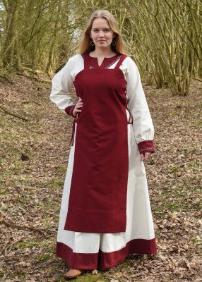 Tablier viking Tinna rouge porté sur une robe blanche, avec coupe ouverte et laçage latéral pour reconstitution, GN ou LARP