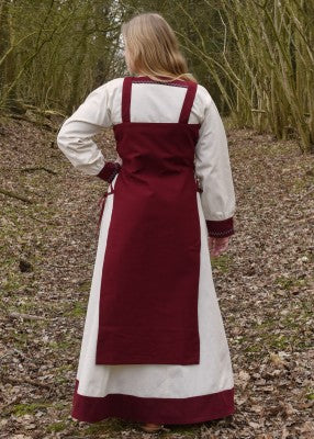 Vue de dos du tablier viking Tinna rouge, porté sur une robe blanche avec coupe ouverte et dos droit