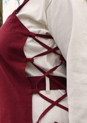 Détail du laçage latéral du tablier viking Tinna rouge, porté sur une robe blanche