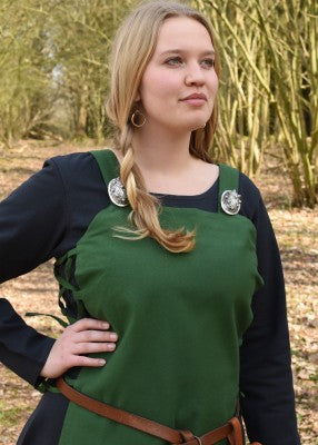 Détail du tablier viking Tinna vert porté sur une robe bleu foncé, avec bretelles droites et fibules décoratives