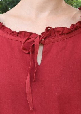 Détail de l’encolure de la tunique Birga rouge, avec petite ruche et lien de fermeture